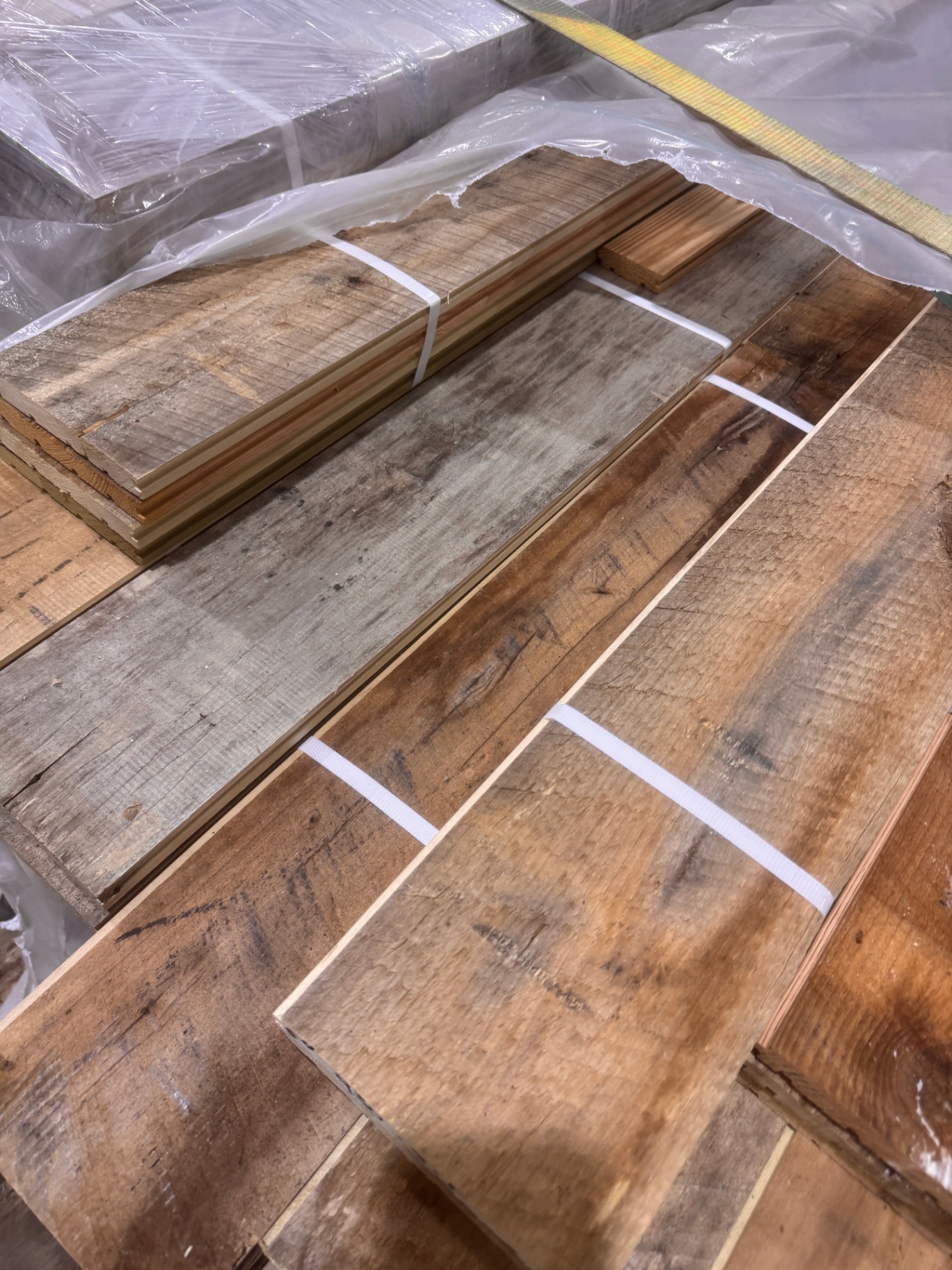 Bundles of milled reclaimed lumber in mixed weathered tones under protective wrap