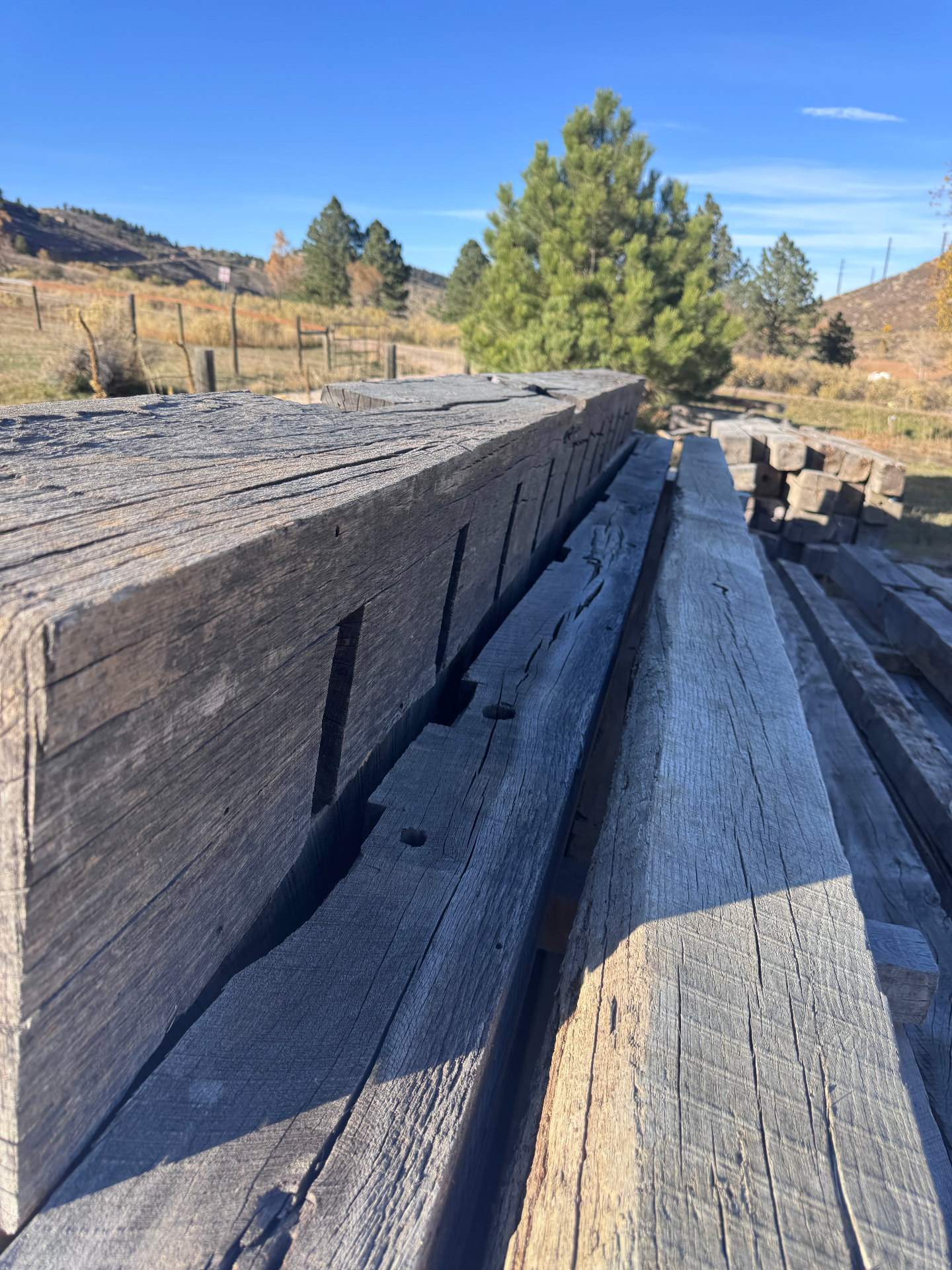 Long row of rough sawn beams stacked outdoors with mountain backdrop