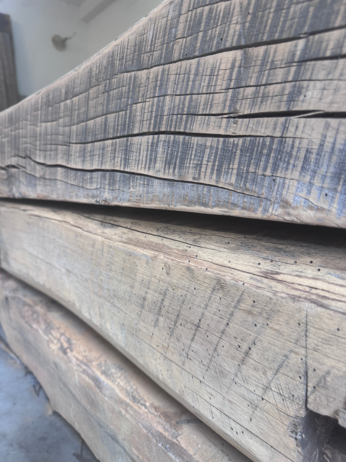 Edge profile of stacked sanded reclaimed beams showing soft saw-kerf shadows and silver-brown patina