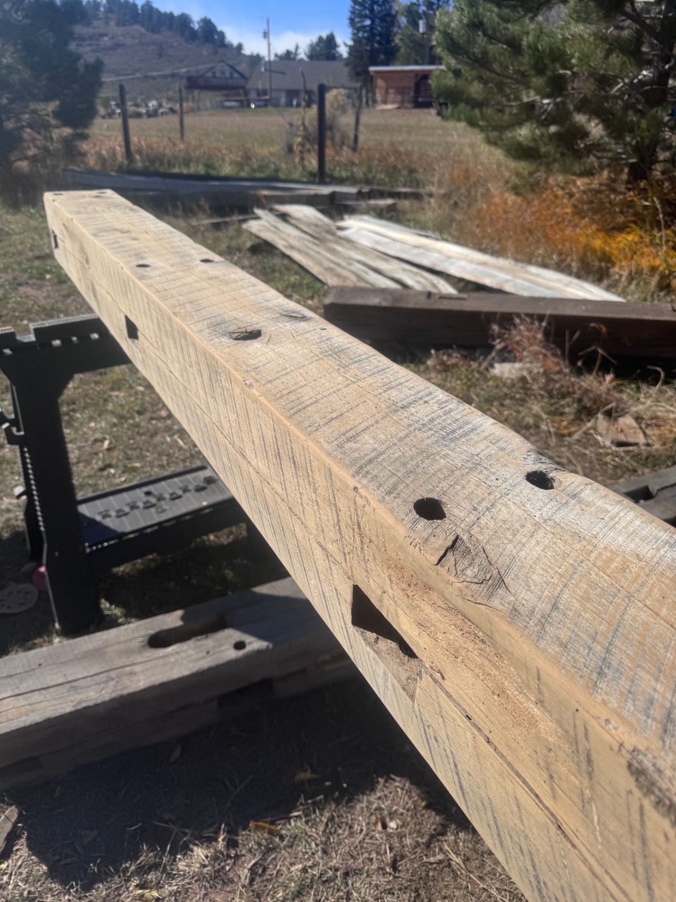 Sanded reclaimed beam with peg holes and mortise pocket on sawhorse outdoors