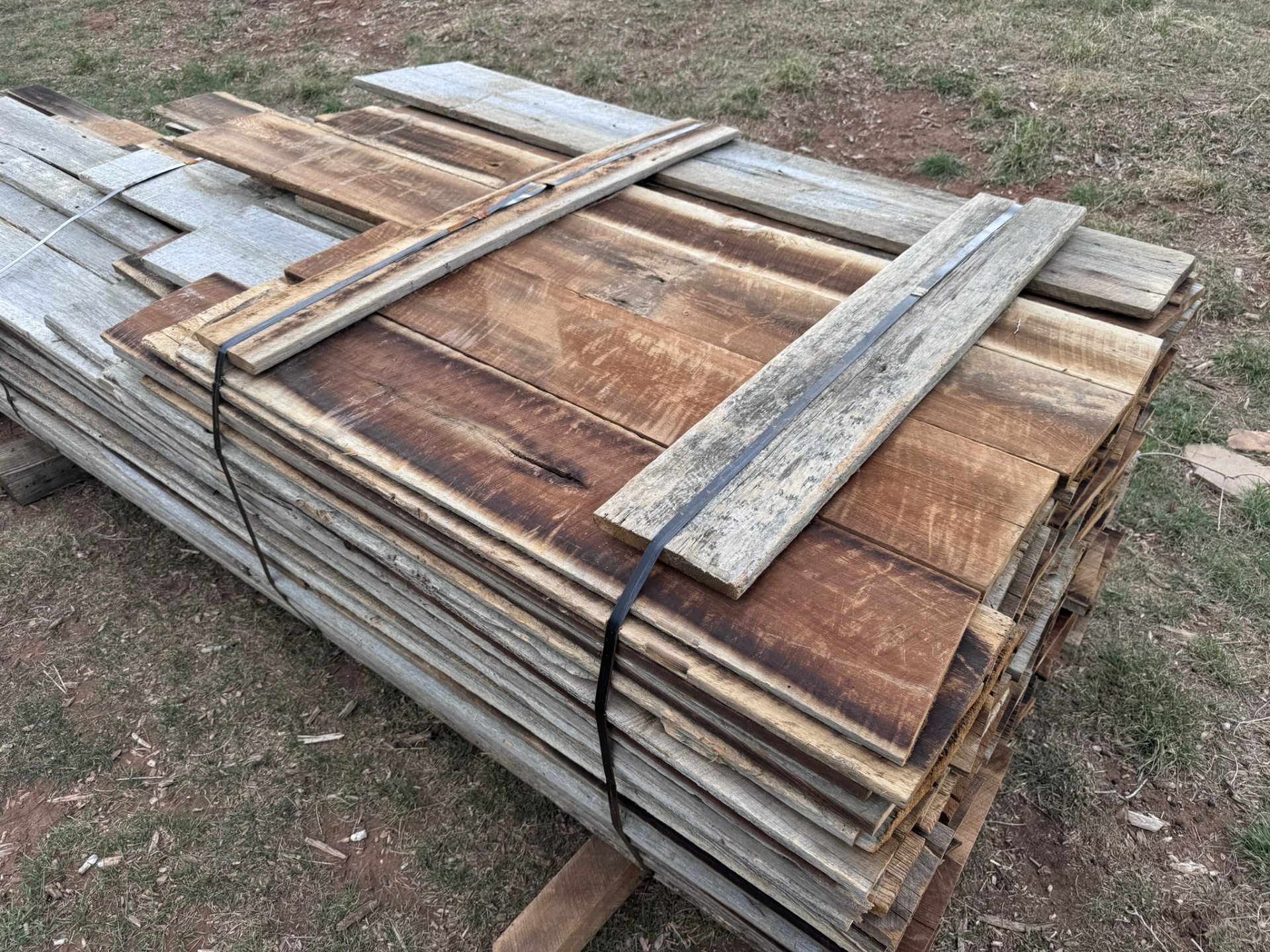 Bundle of mixed-tone reclaimed barnwood siding boards strapped on pallet