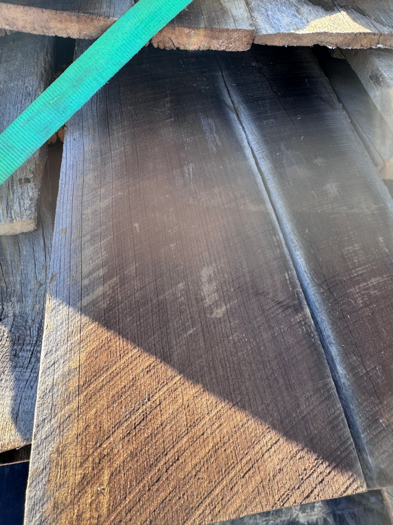 Dark-toned reclaimed barnwood siding boards strapped with green tie-down