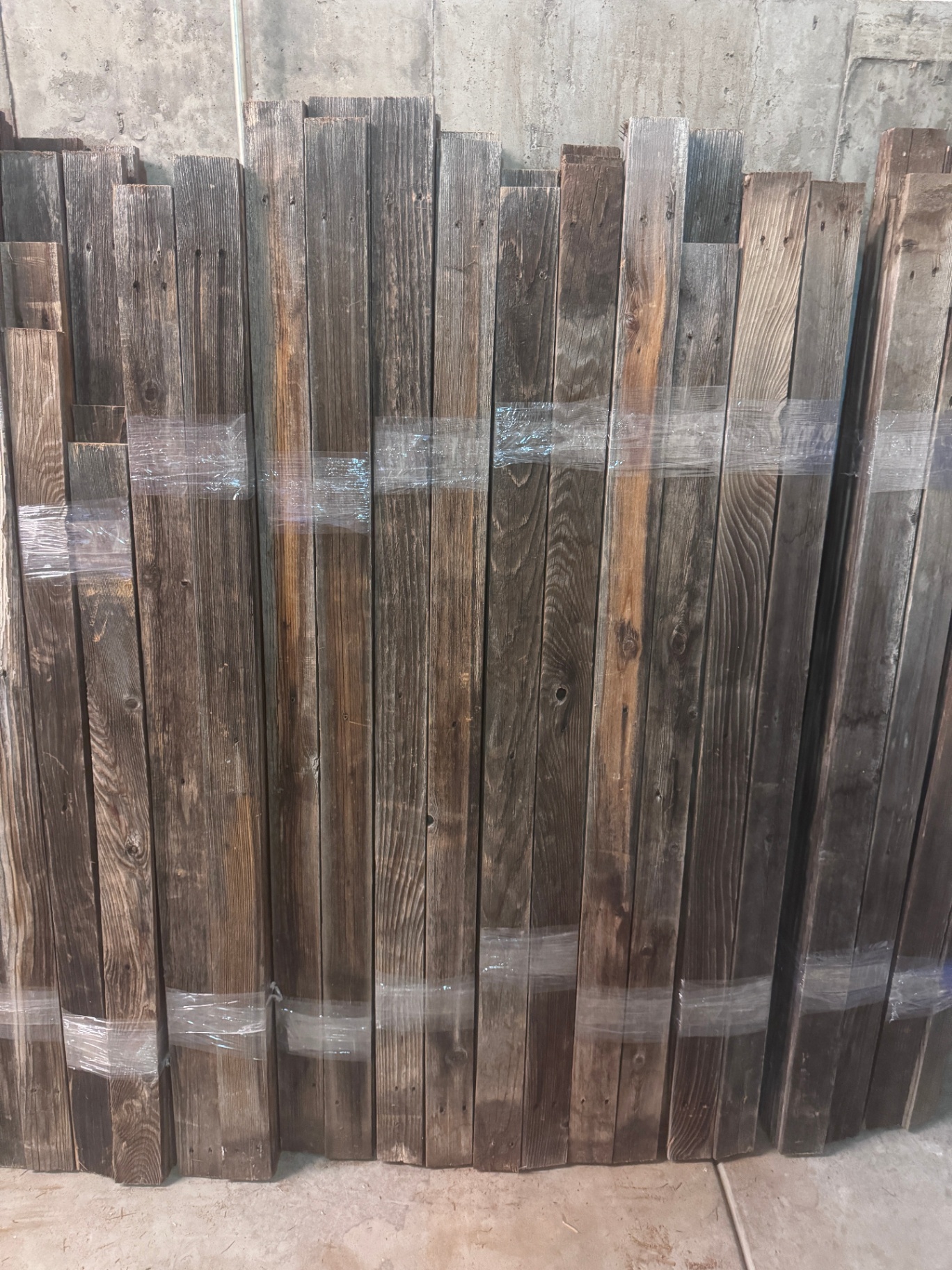 Stacked bundle of reclaimed Colorado snow fence boards leaning against concrete wall